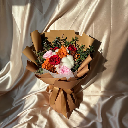 seven stunning roses in shades of pink, red, and orange. Wrapped in a sophisticated reddish-brown paper, this preserved bouquet exudes elegance and charm. 